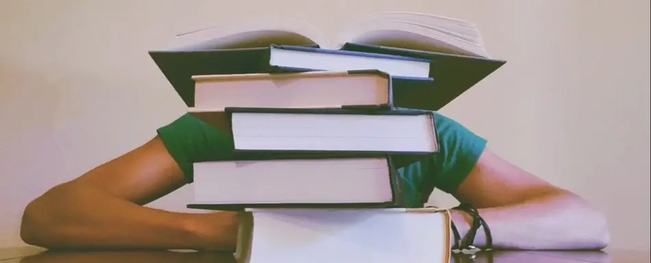 A person's face hidden behind a stack of books.