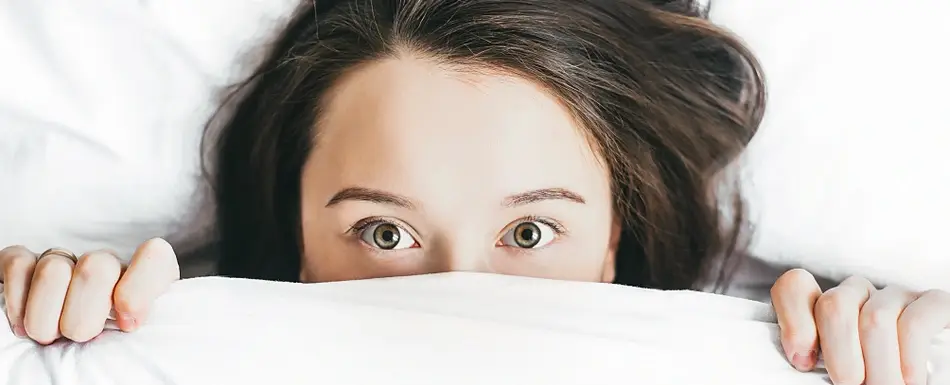 woman in bed hiding face under covers