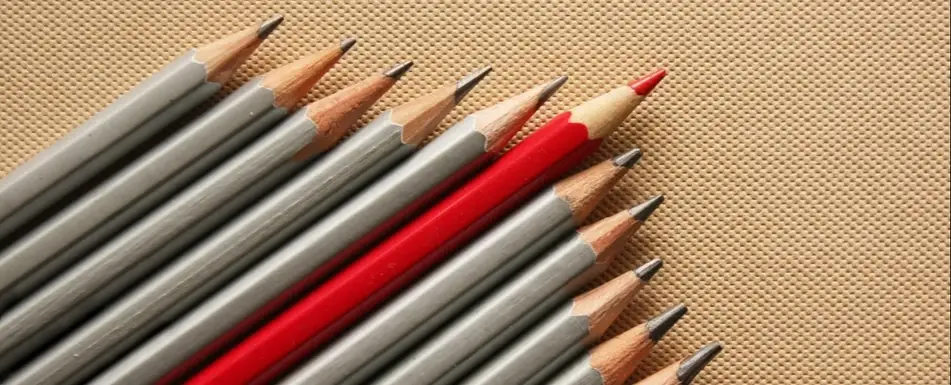 A group of grey pencils and one red crayon pencil in the middle.