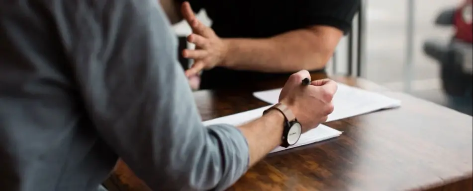 Two people sitting on a table discussing. One is writing on a piece of paper.