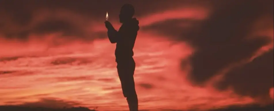 A man holds a flame under a red sky.
