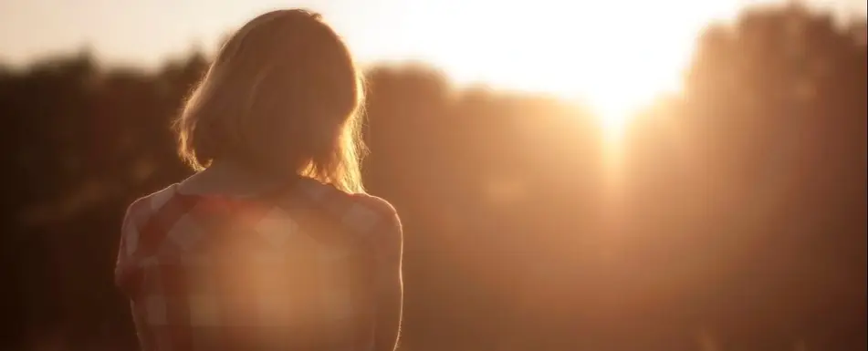 A woman looks out at a sunset.