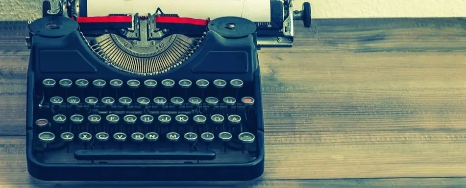 A close up of a typewriter sitting on a wooden desk.