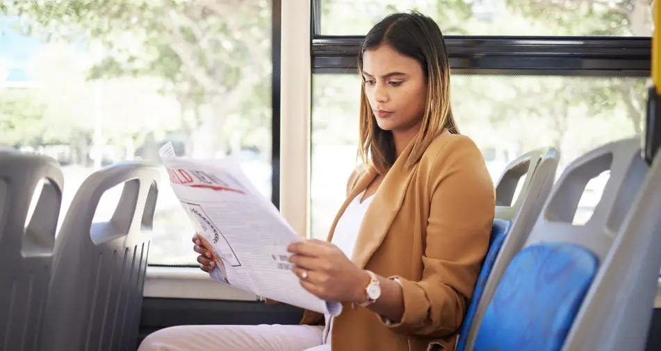 A woman rides public transportation on her way to a job interview, reading a newspaper.