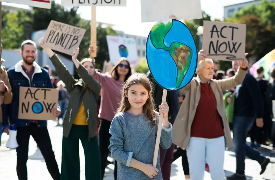 A little girl holds up a sign of planet earth with other protestors for climate change stand behind her.