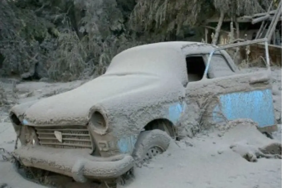 An abandoned car covered in sand on a beach.