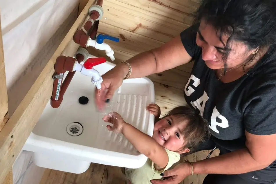 A woman helps a little girl wash her hands in a bathroom sink.