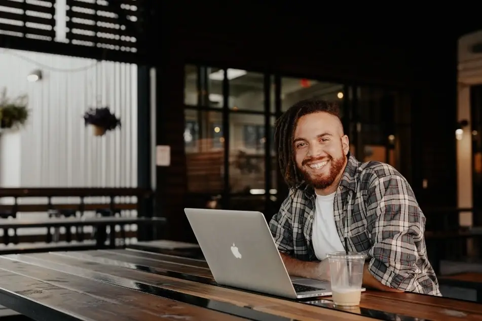 Hombre joven en un café sonriendo con una computador portátil