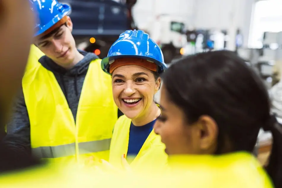 Photograph of a white woman smiling with her co-workers, who are all wearing yellow vests and blue construction hats.