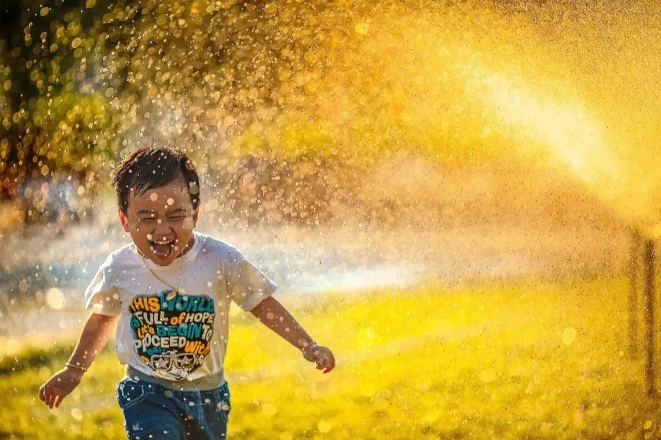 Niño feliz corriendo frente a un riego de agua