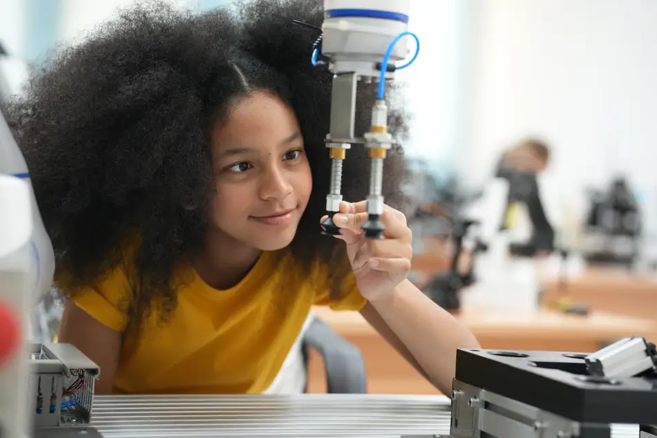 A young Black girl sits at a desk in a school, looking at a instrument in science class. Behind her are microscopes and other scientific instruments.