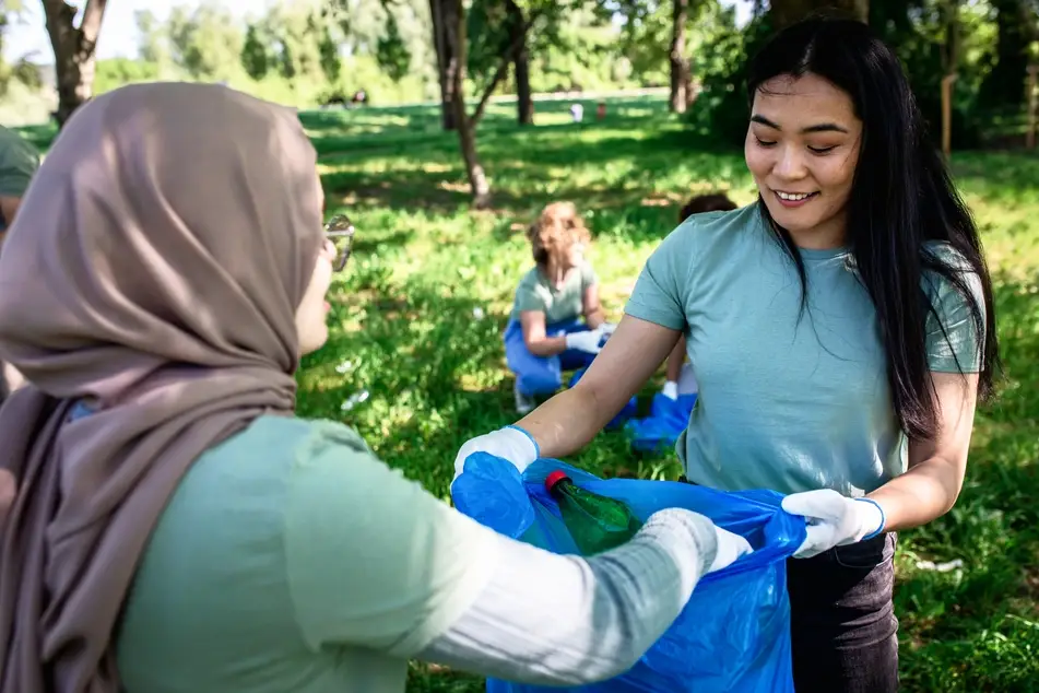 A group of volunteers gathers trash in a green park as part of their social-impact work.