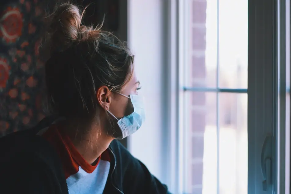 A person with a bun looks out the window with their mask on.