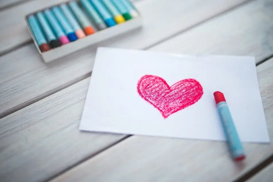 A box of crayons and piece of paper with a heart drawn on it.