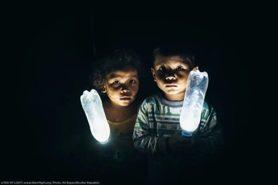 Um menino e uma menina, no escuro, com garrafas plásticas que emanam luz do seu interior