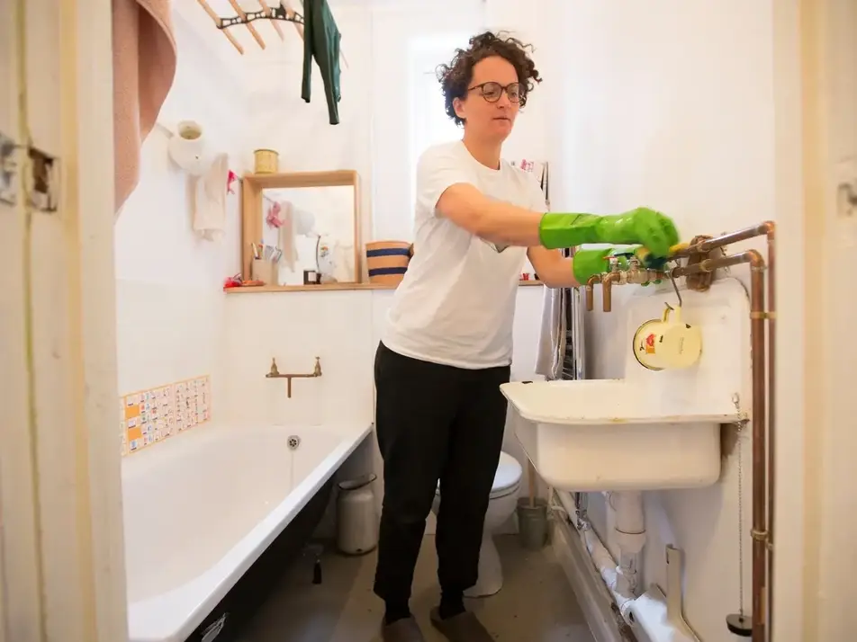 A person cleans their bathroom while wearing green gloves.