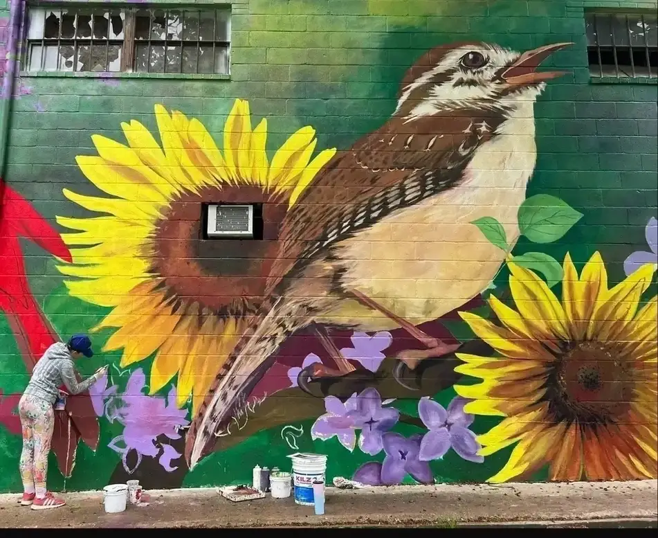 Persona pintando un mural sobre naturaleza en una pared