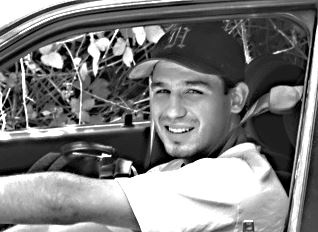 Young man in baseball cap sits in car and smiles at camera