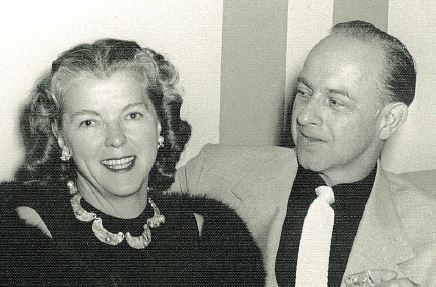 Woman in black dress smiles at camera and man on her right looks at her