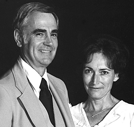 A tall man in a suit and a shorter brunette woman smile at camera
