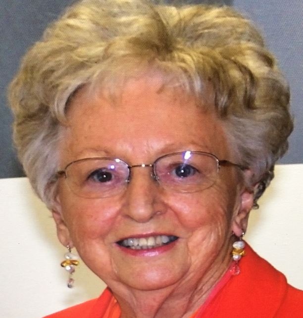 Older blonde woman in red shirt with square glasses and earrings smiling at camera