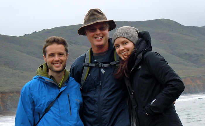 Three people smiling at camera and standing in front of a lake and green mountainside