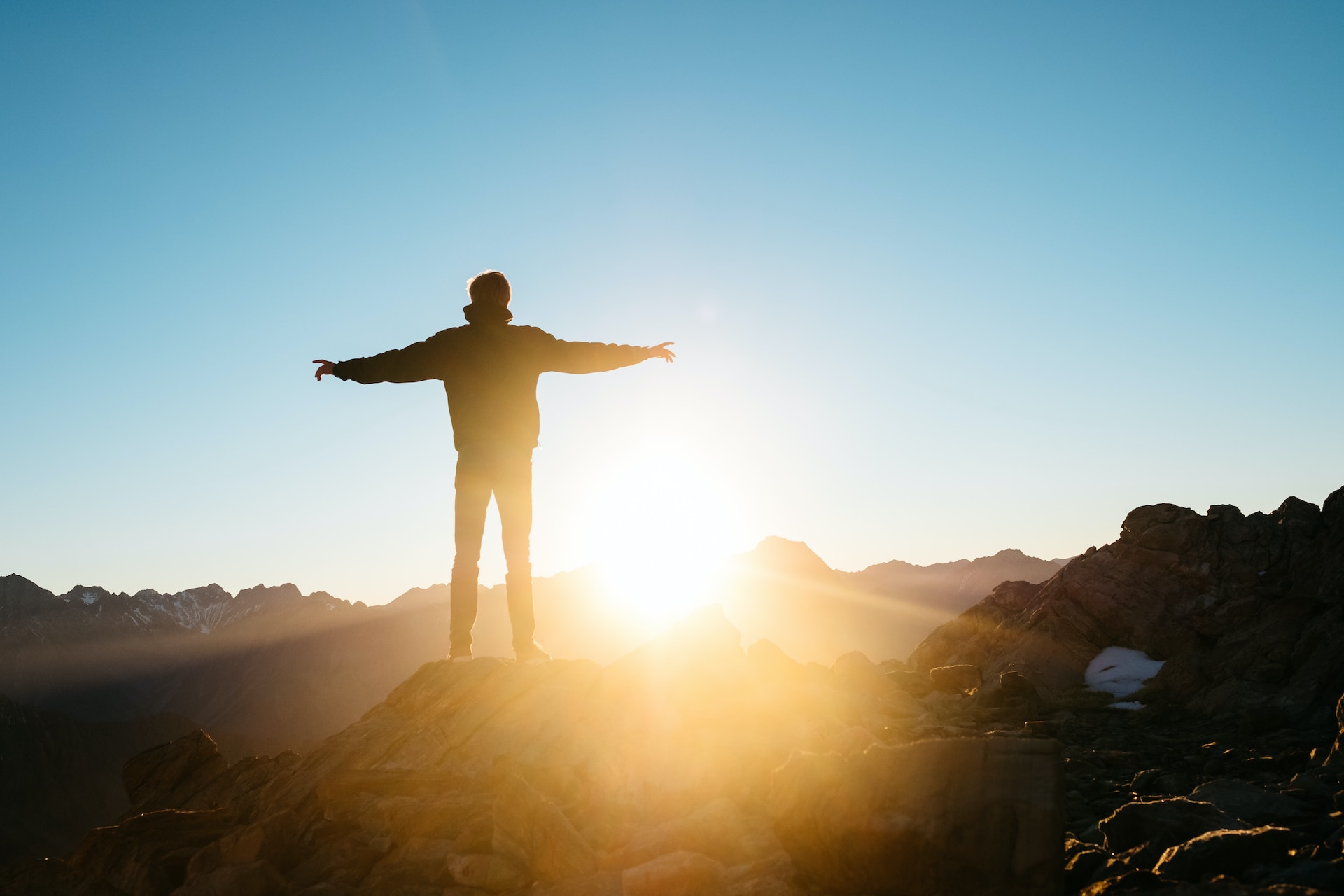 a man standing on a mountain with opening hand looking at the sun stock image