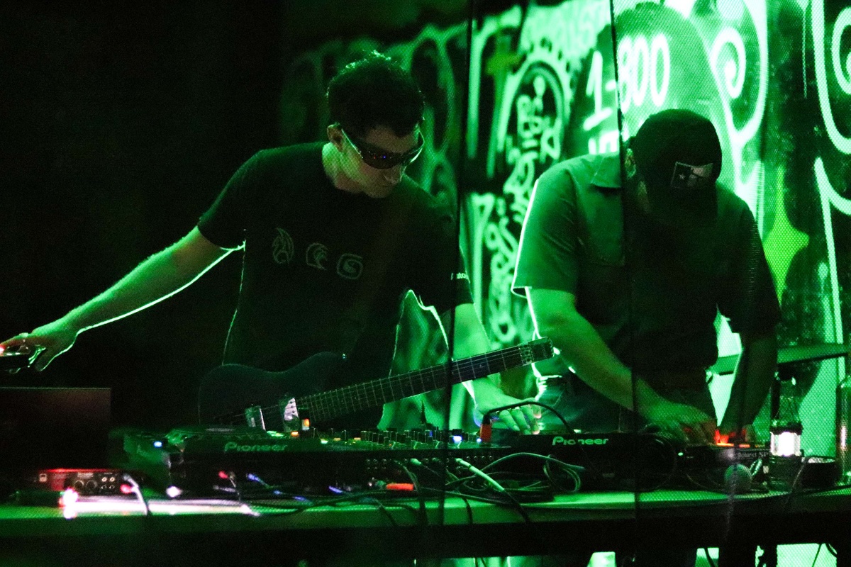 two people stand over a DJ table bathed in green light