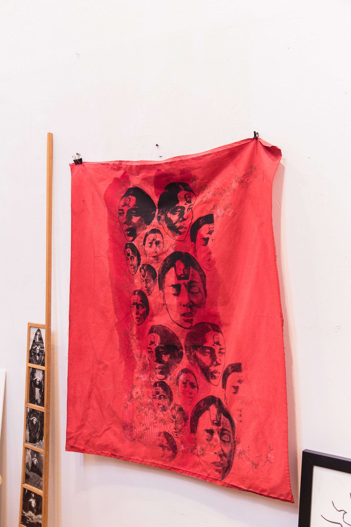 A red silk print of Ana Mendieta made by Mary Beth Edelson hangs on a white wall.