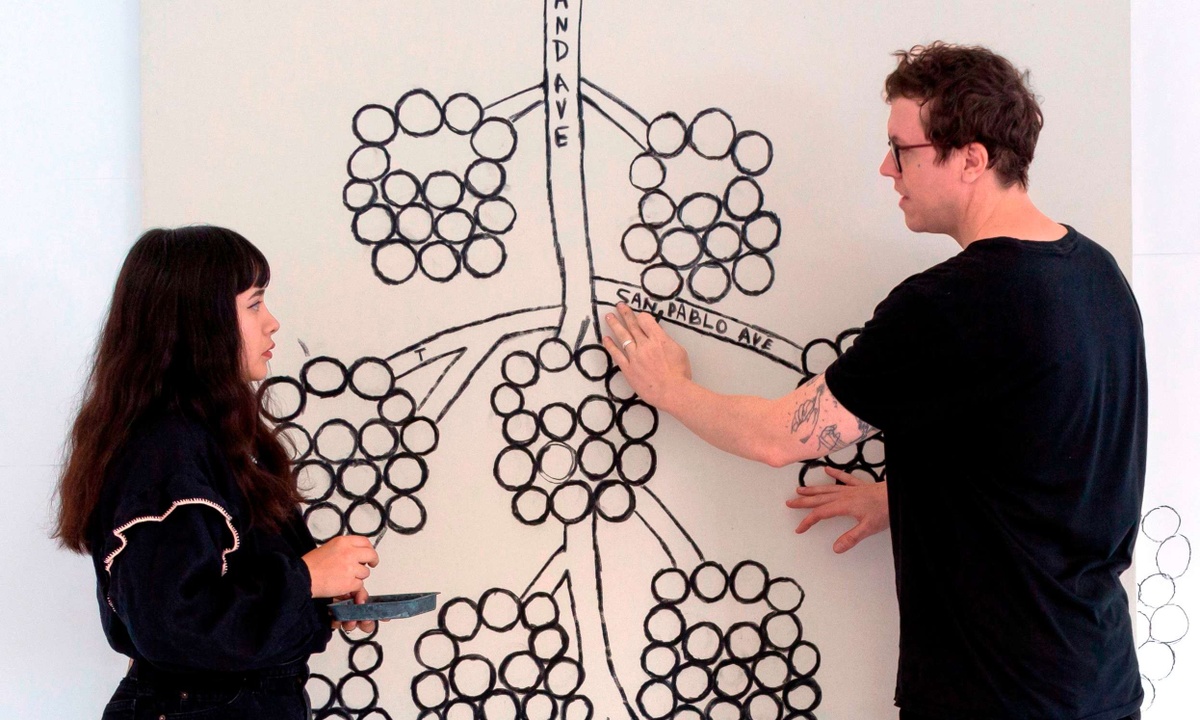 Liz Hernández and Ryan Whelan standing in front of a large black and white artwork with abstract blackberries