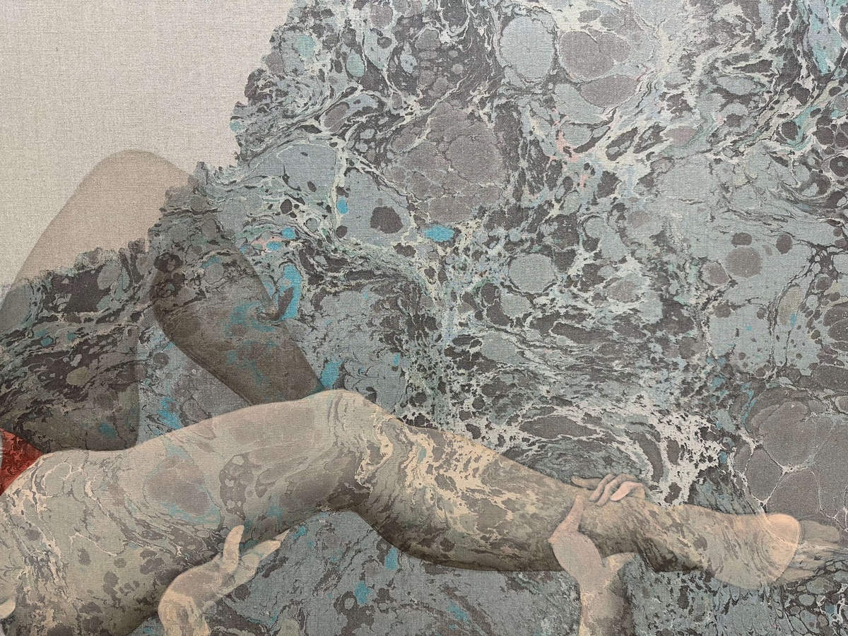 Two pale legs fill the bottom half of the composition, supported by two pale hands emerging from the bottom edge. The background is a raw beige linen, with blue and gray marbling covering all but the top left corner.