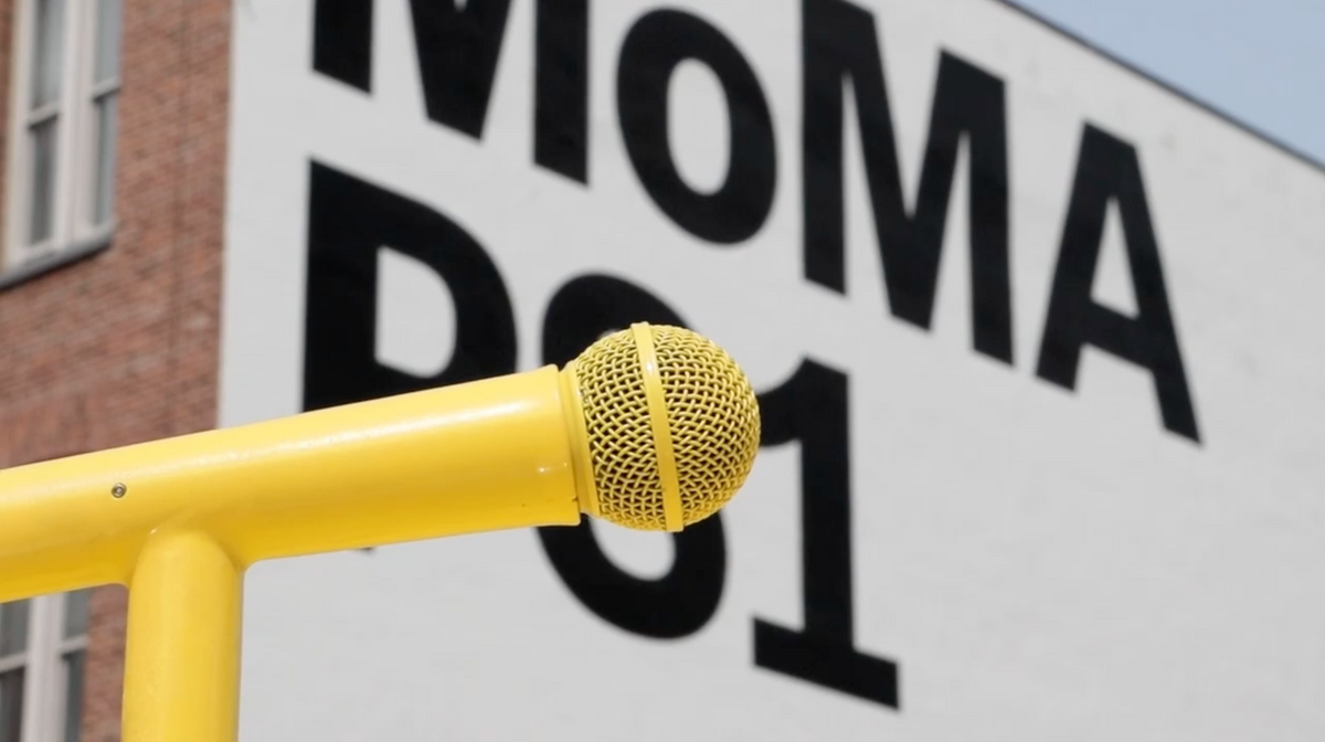 Video pans over a yellow microphone. In the background is a building wall painted with the words "MoMA PS1."