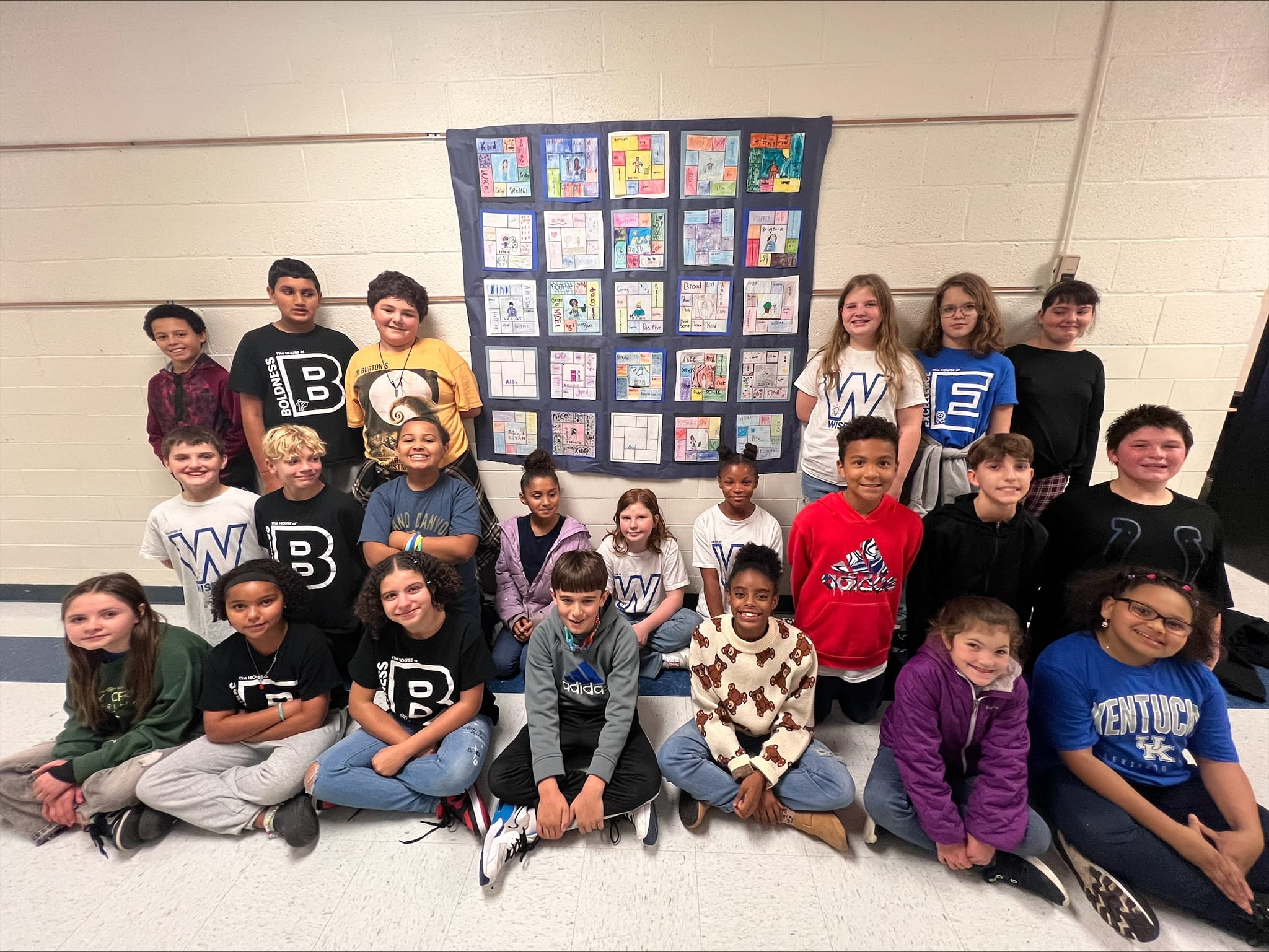 22 people post with paper quilt hanging on wall.