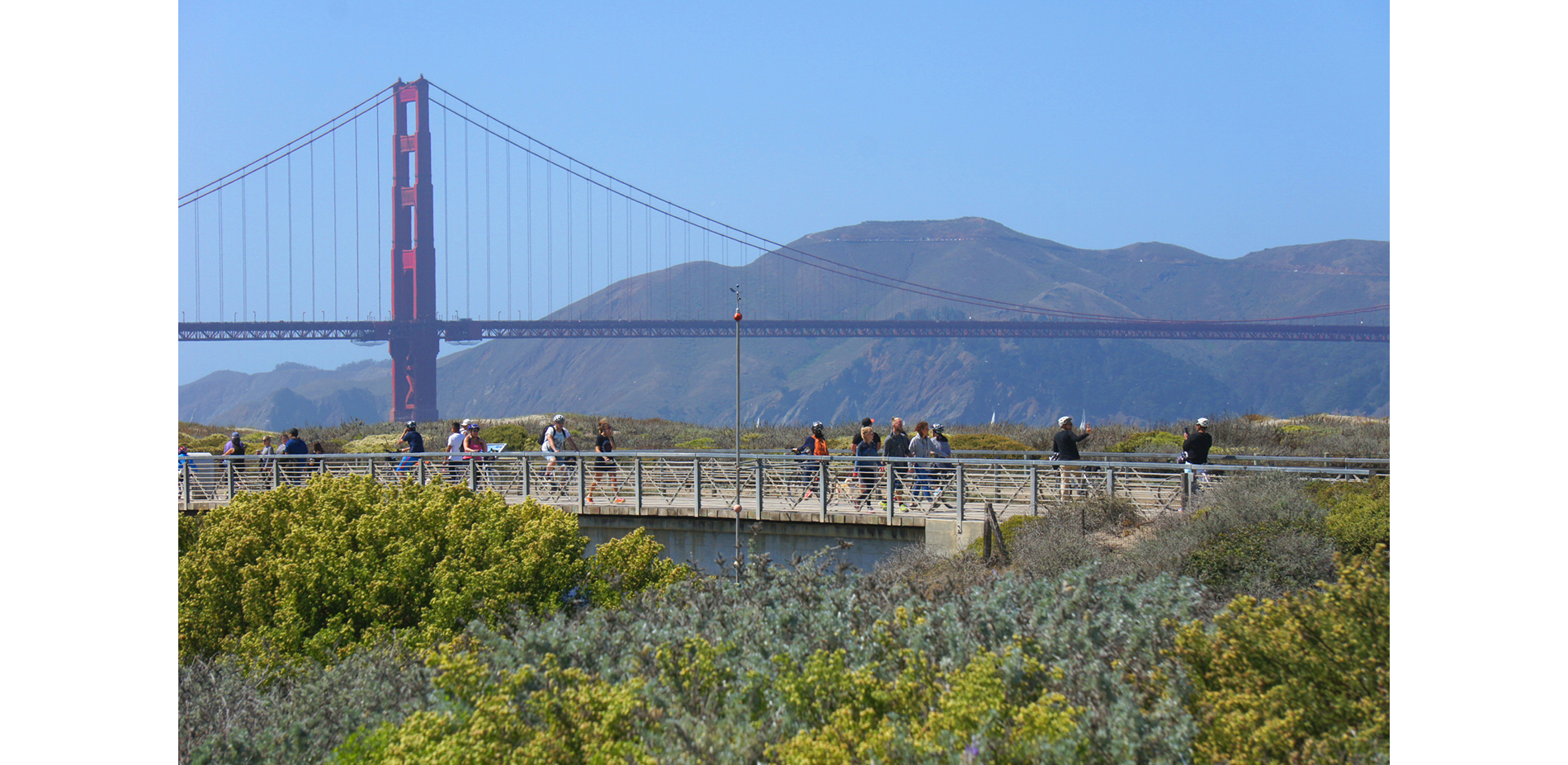 Pedestrian bridge over the marsh inlet connects visitors to daily tidal dynamics against an iconic background.