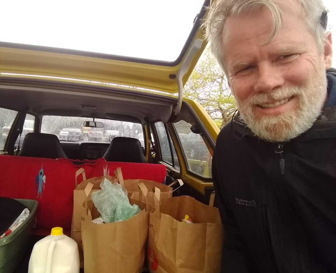 Homem com compras e mantimentos no porta-malas do carro