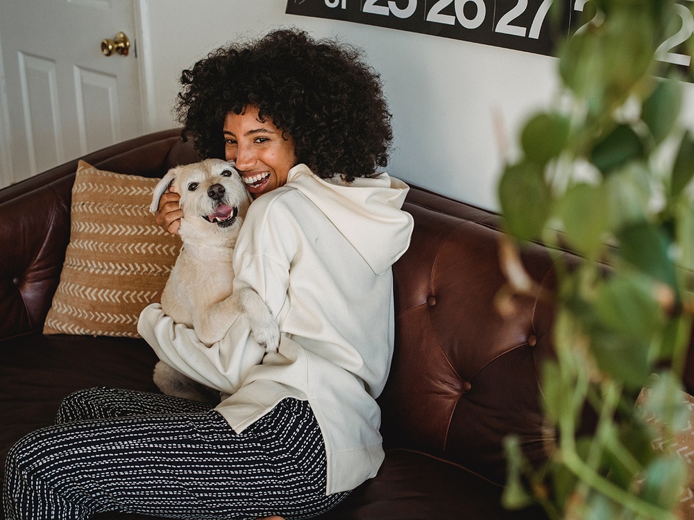 A woman cuddles with her new dog on a brown leather sofa. Both are obviously happy.