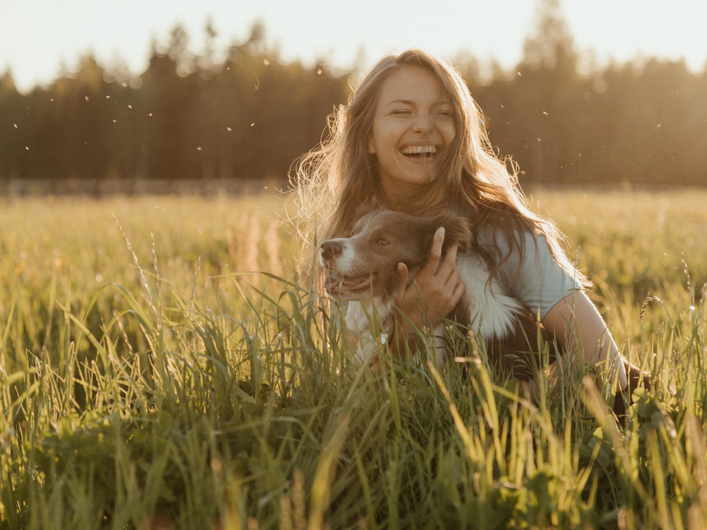 A happy dog is hugged by a woman pet sitter in a sun soaked field.