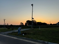 A shadowy Joplin Schools facility crew member digs landscaping materials at dawn.