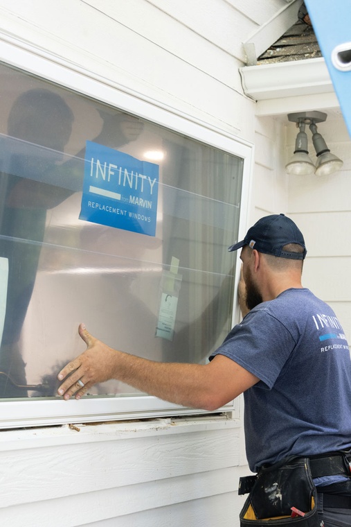 An Infinity from Marvin window installer places a large white window into a frame for installation.