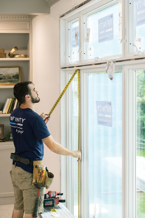 A window installer uses a tape measure to check the height of an installed window.