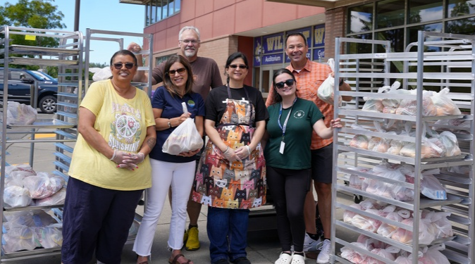 food service workers and district staff standing with packaged summer meals for families