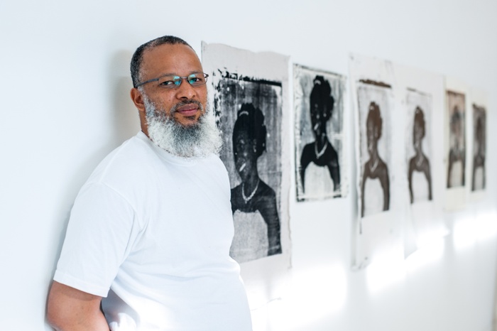 Newly appointed Associate Professor in Painting/Printmaking Meleko Mokgosi against a white gallery wall featuring series of black and white portraits.