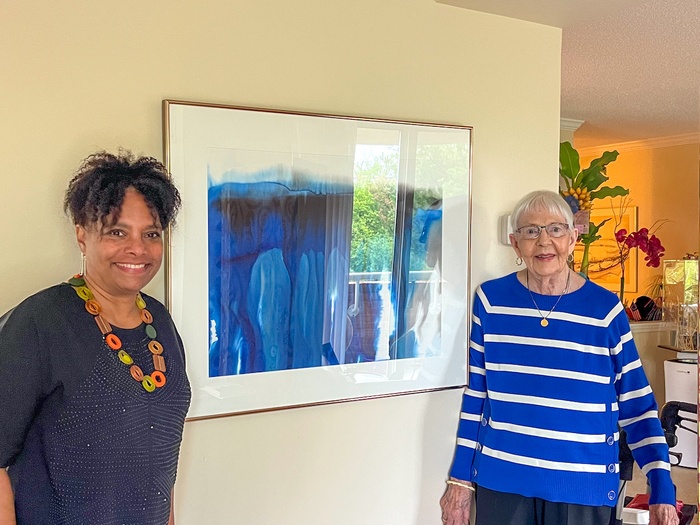 Two women in front of a framed blue watercolor.