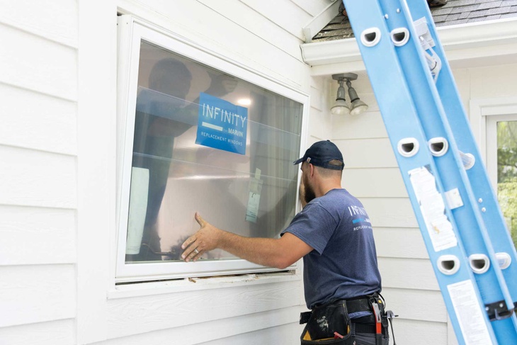 An Infinity from Marvin window installer places a large white window into a frame on a home.