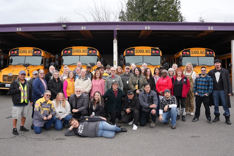 group of bus drivers standing in front of a row of school busses