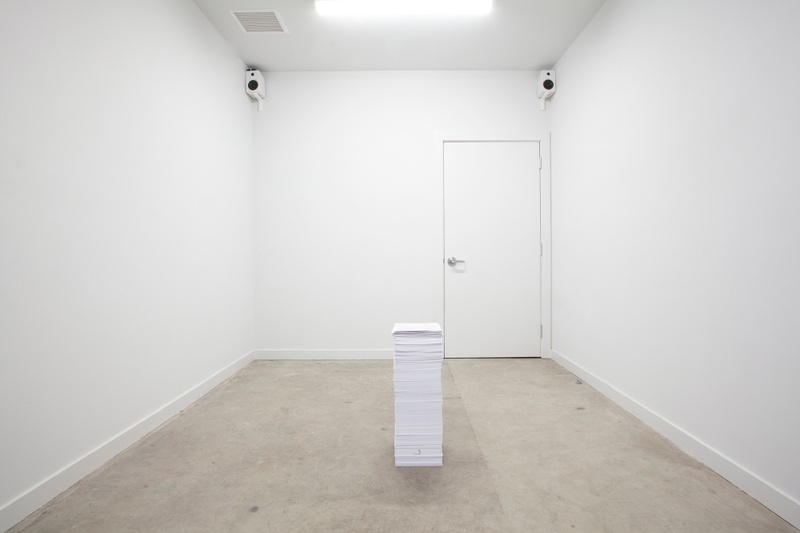 In the center of a room with white walls and a grey floor is a four foot tall stack of papers, consisting of medical bills and a life-care plan. In two corners of the room are speakers that play instrumental hold-tone music.