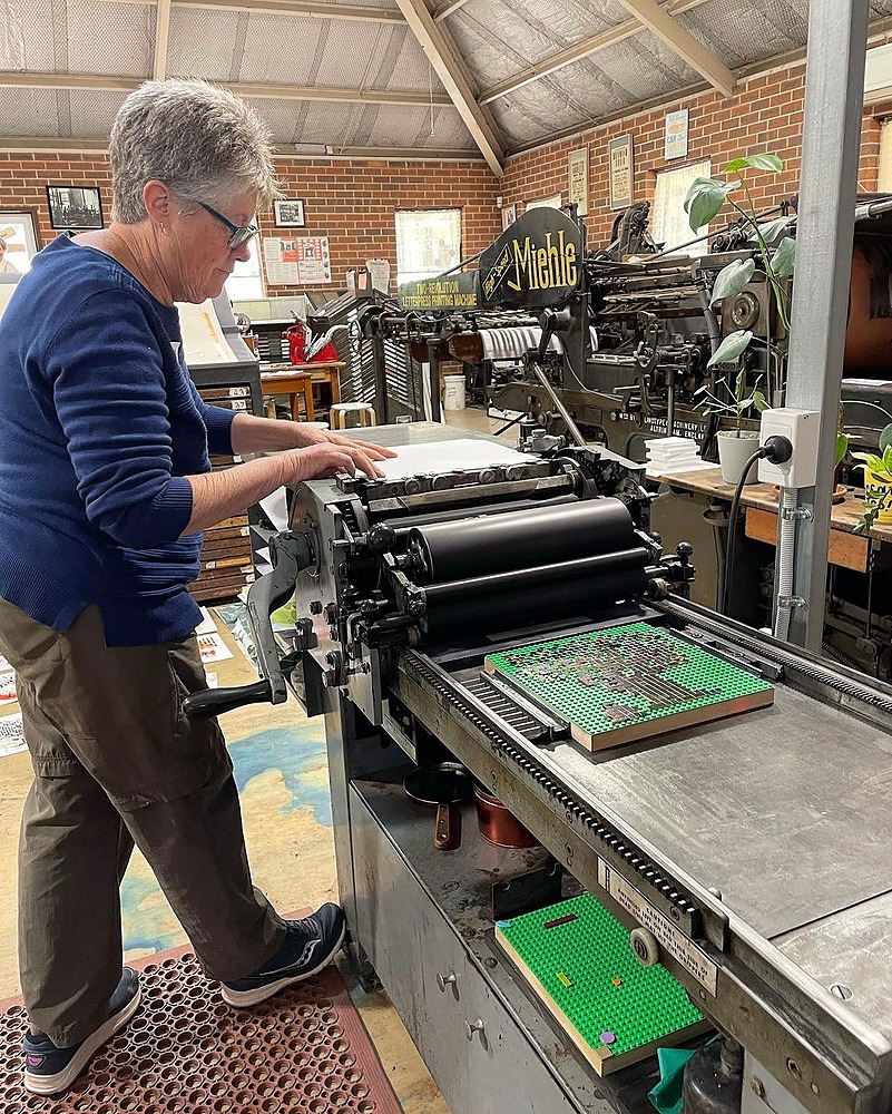 A participant feeding paper on the Vandercook press getting ready to print