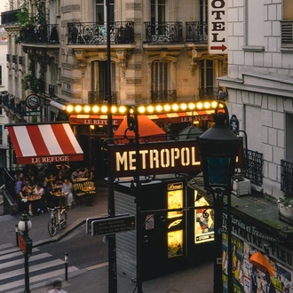 A wide view of a typical city street in Paris, with a busy restaurant and a sign for the Paris metro in view.