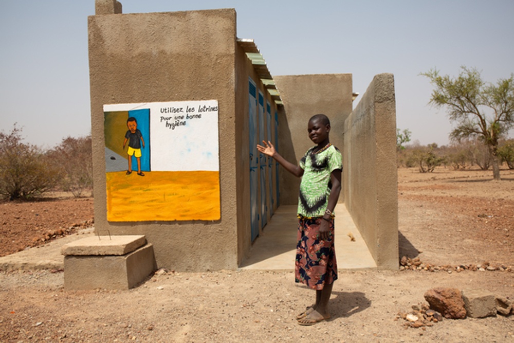 Simonda Ndaboi, 18, framför toaletterna för flickor på Lipumpu Secondary School, Mwandi District, Zambia, februari 2022. Bild: WaterAid/ Chileshe Chanda.