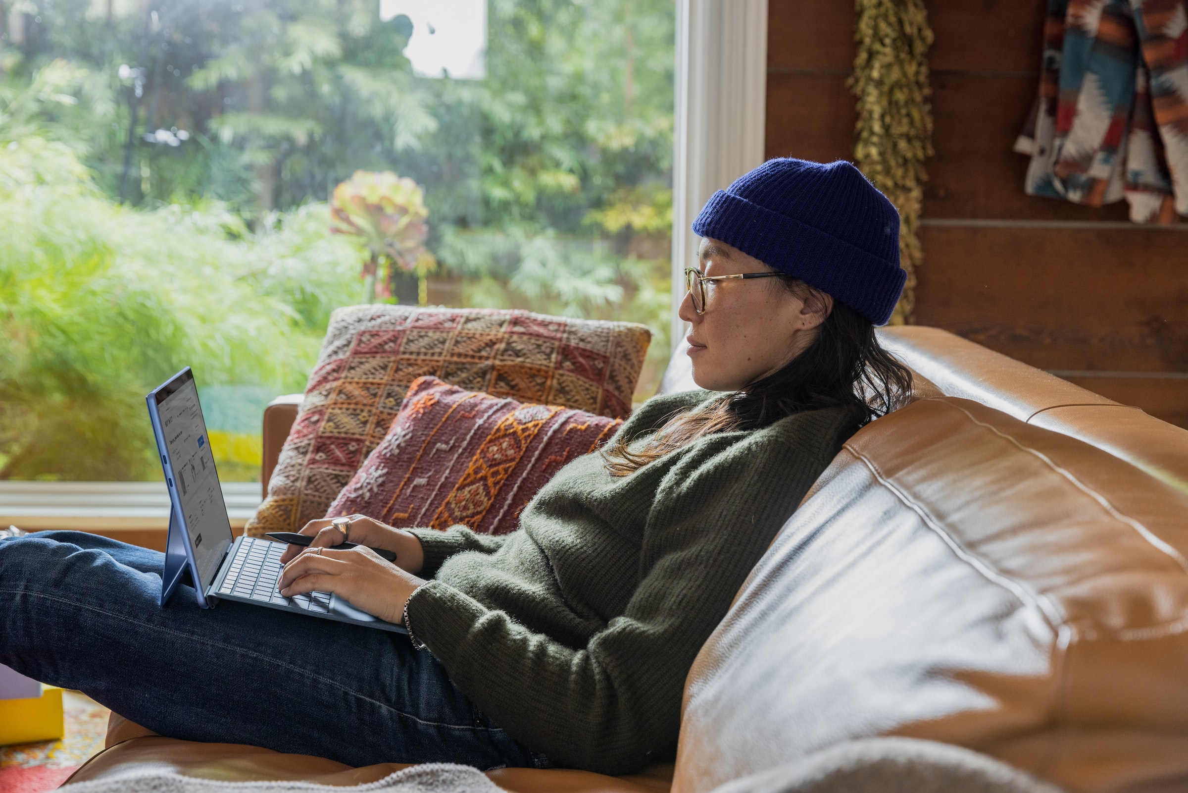 asian woman sits on a sofa while working with an ipad, a keyboard, and a stylus stock image